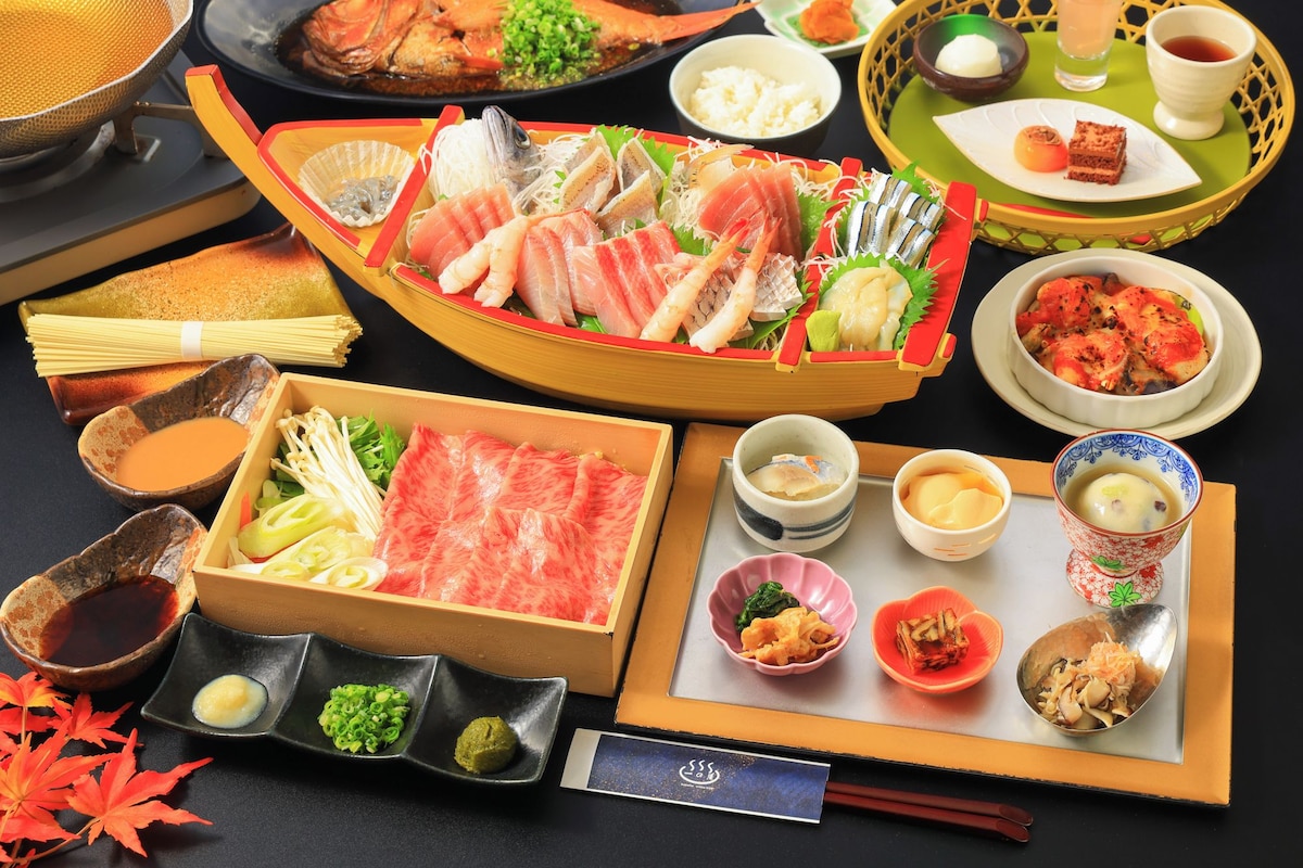 Diversos pratos japoneses, como sashimi, sushi e tempura, dispostos sobre uma mesa com hashis e pequenos recipientes de acompanhamentos.