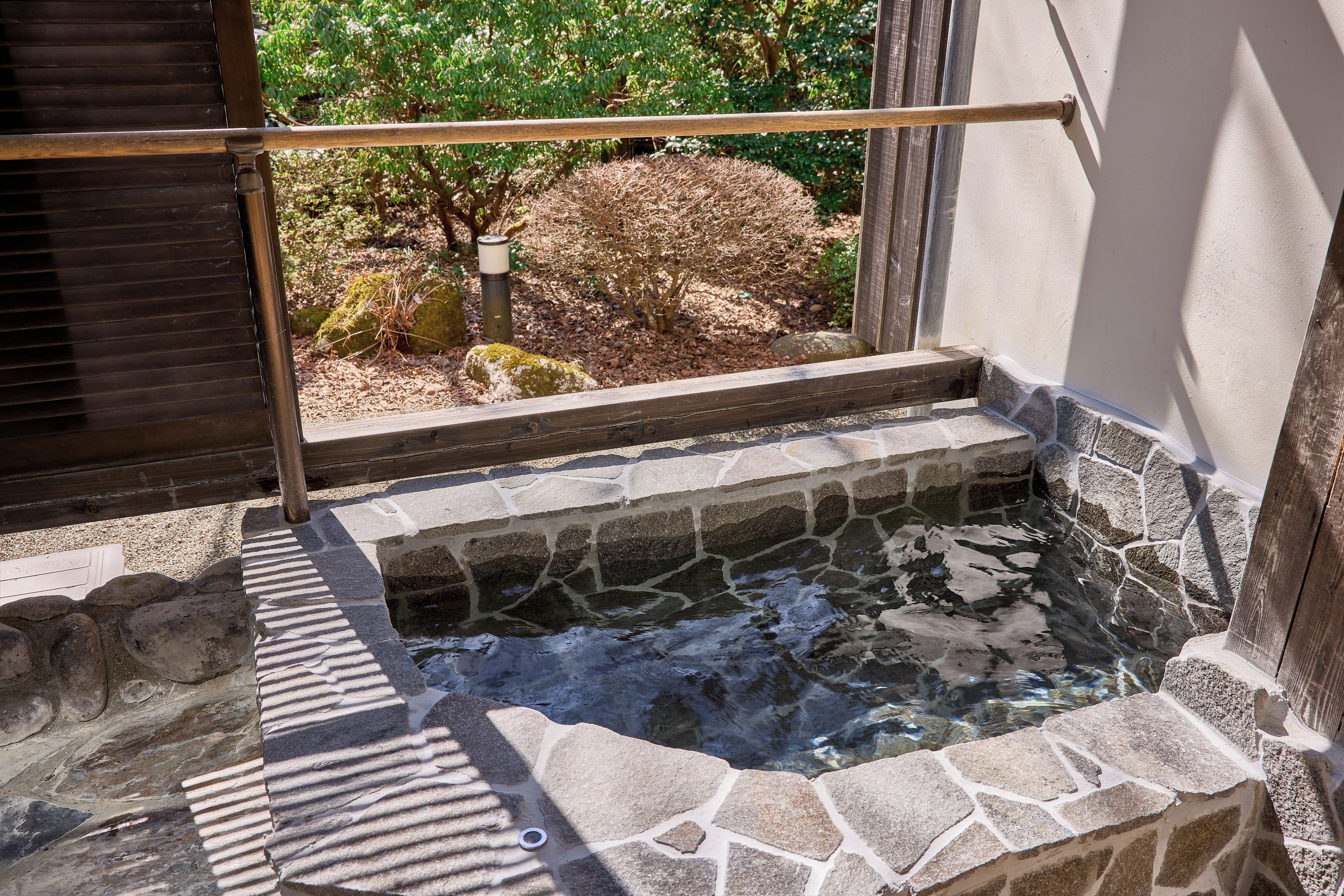 A stone hot spring with a wooden railing, surrounded by stone steps and a stone wall.