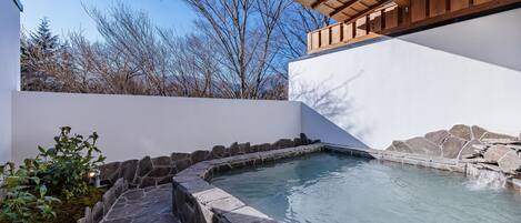 Un área de piscina moderna al aire libre con escalones de piedra que conducen al agua, rodeada por un muro blanco y una pérgola de madera.