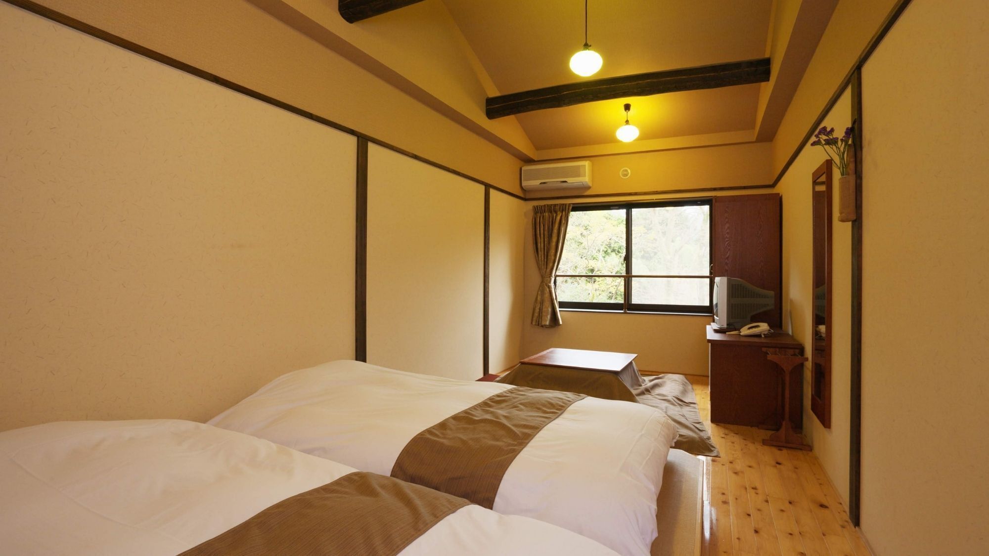 Una habitación con dos camas, un escritorio con teléfono, un equipo de aire acondicionado y una ventana con cortinas.