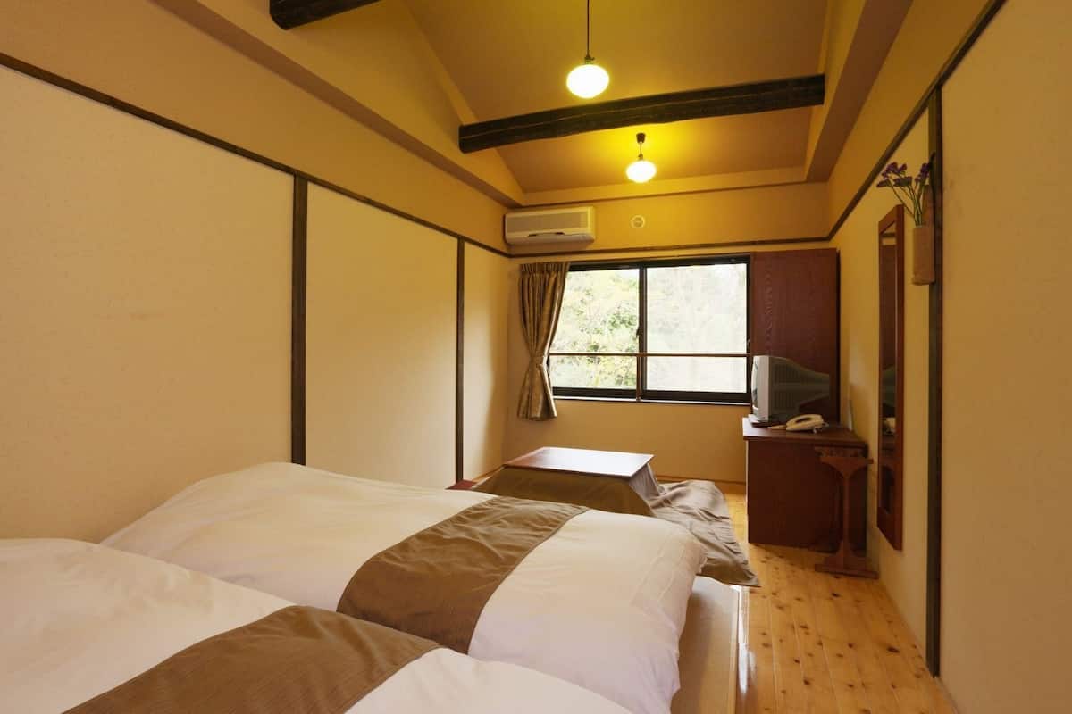 A room with two beds, a desk with a telephone, an air conditioning unit, and a window with curtains.