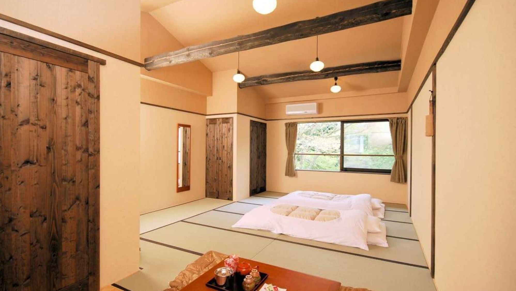 Una habitación japonesa tradicional con suelo de tatami, futón, puertas correderas de madera y ventana con vistas.