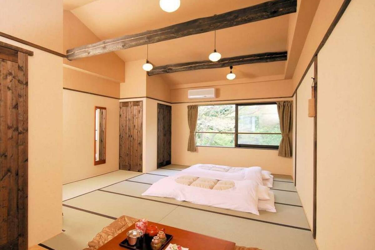 A traditional Japanese room with tatami flooring, a futon bed, wooden sliding doors, and a window with a view.