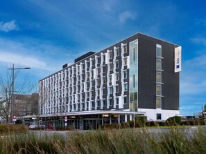 A modern hotel building with a grid-like facade, large windows, and a prominent logo on the side. - ibis budget Auckland Airport (Auckland)