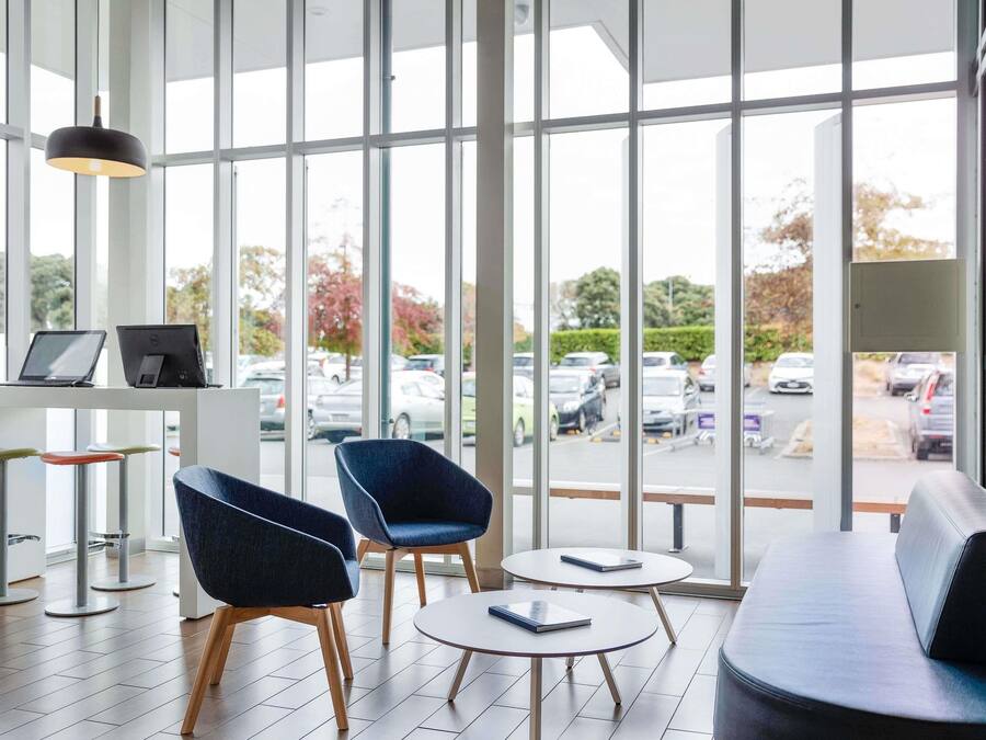 A modern interior with large windows, a seating area, and a table with laptops.