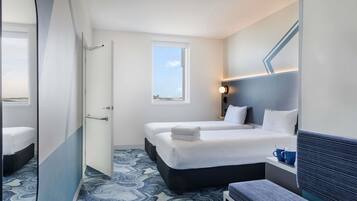 Ett hotellrum med två sängar, en bänk, ett fönster och en väggmonterad lampa.