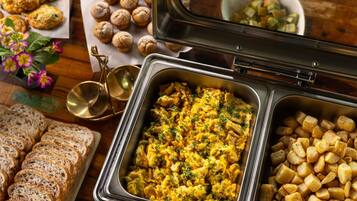 A buffet table with various food items including scrambled eggs, roasted potatoes, and bread.
