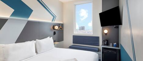 Una habitación de hotel moderna con una cama, un escritorio, un televisor y una ventana con vista a la ciudad.