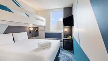 A hotel room with a bed, a TV, a desk, and a window.