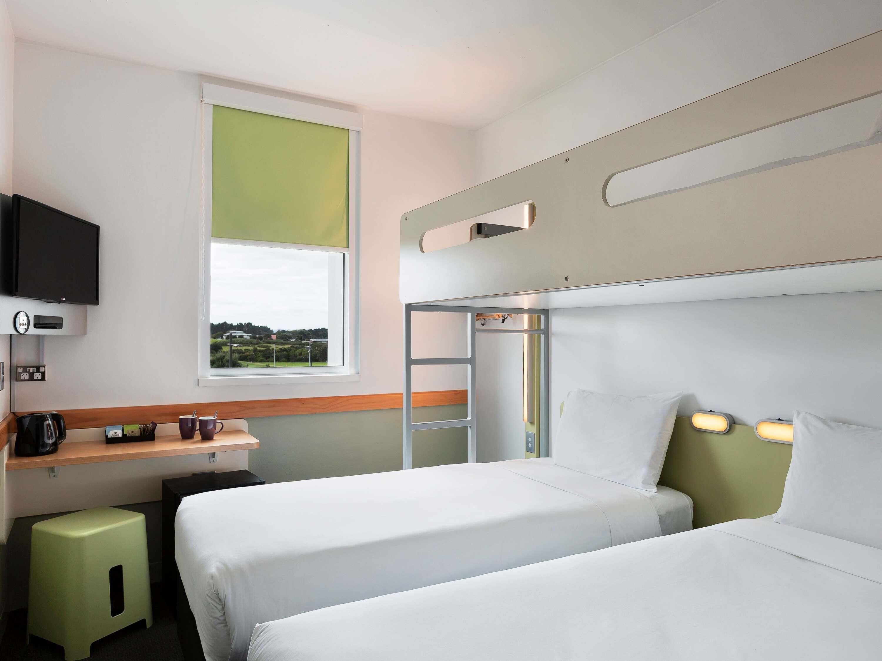 A hotel room with two beds, a desk, a television, and a window with a view.
