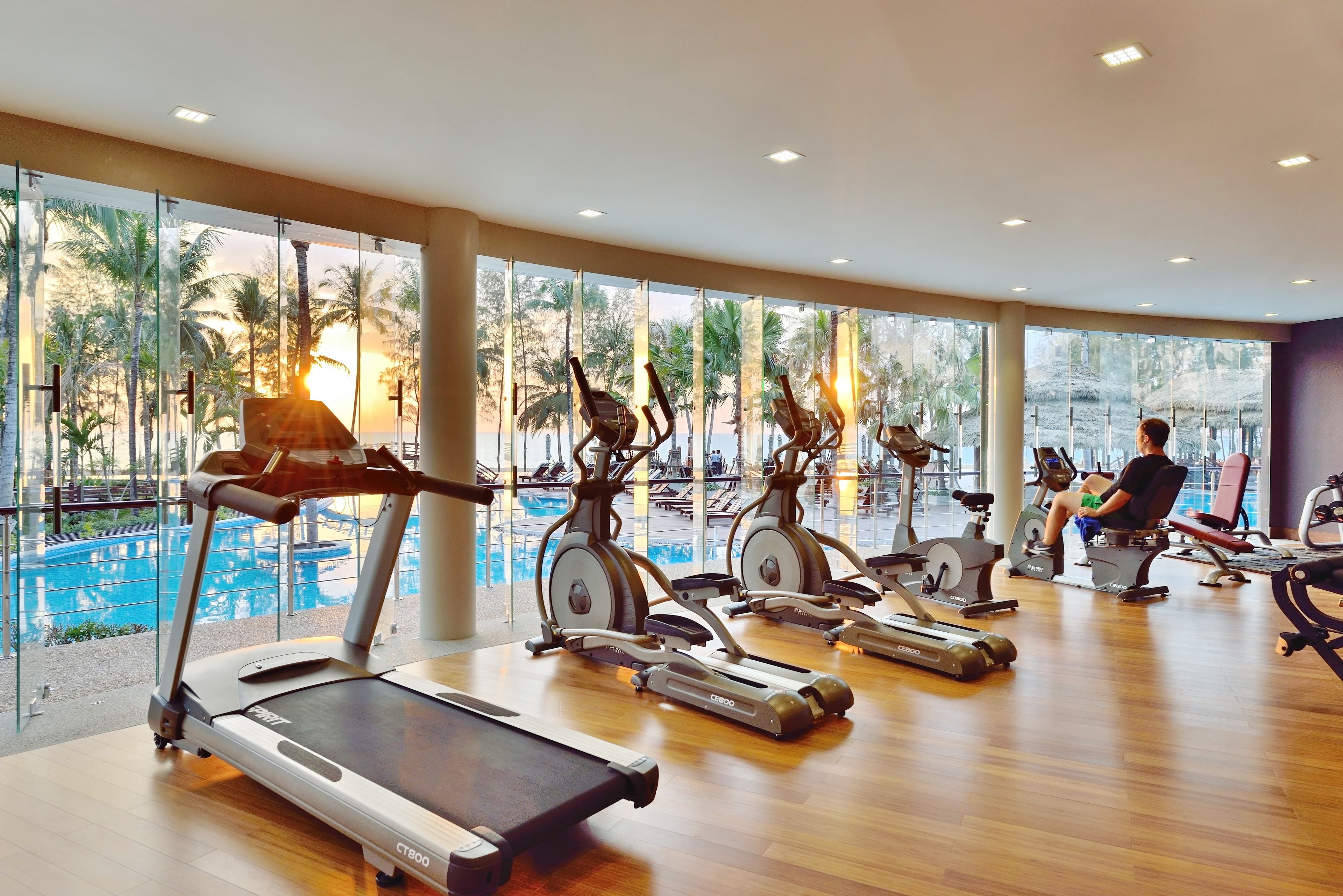 A gym with treadmills and stationary bikes, large windows with a view of palm trees and a pool.