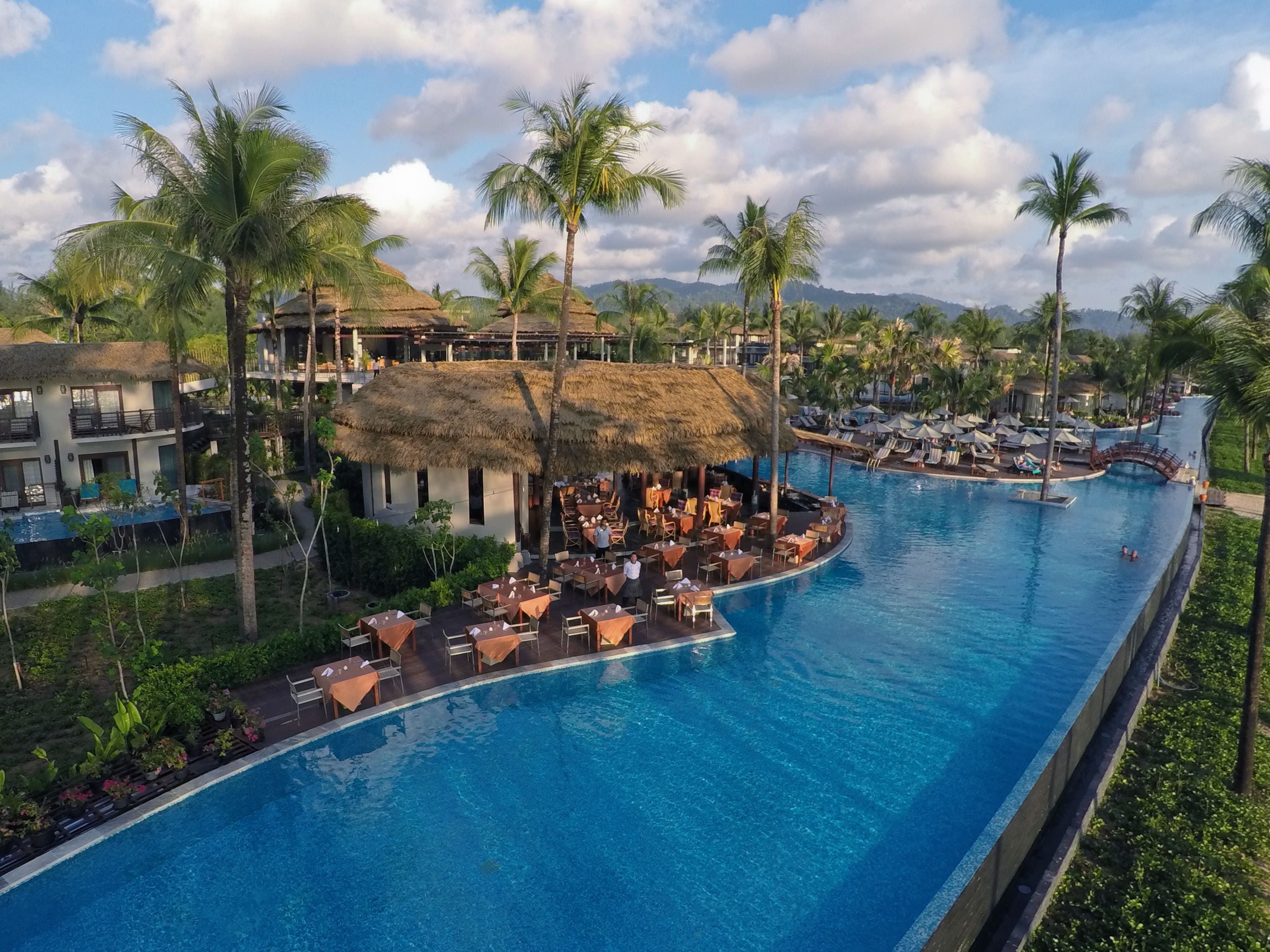 Un resort con una amplia piscina, edificaciones de techo de paja y palmeras.