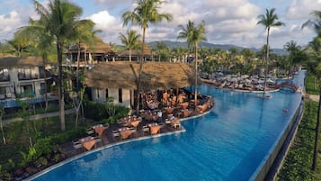 Un resort con una amplia piscina, edificaciones de techo de paja y palmeras.