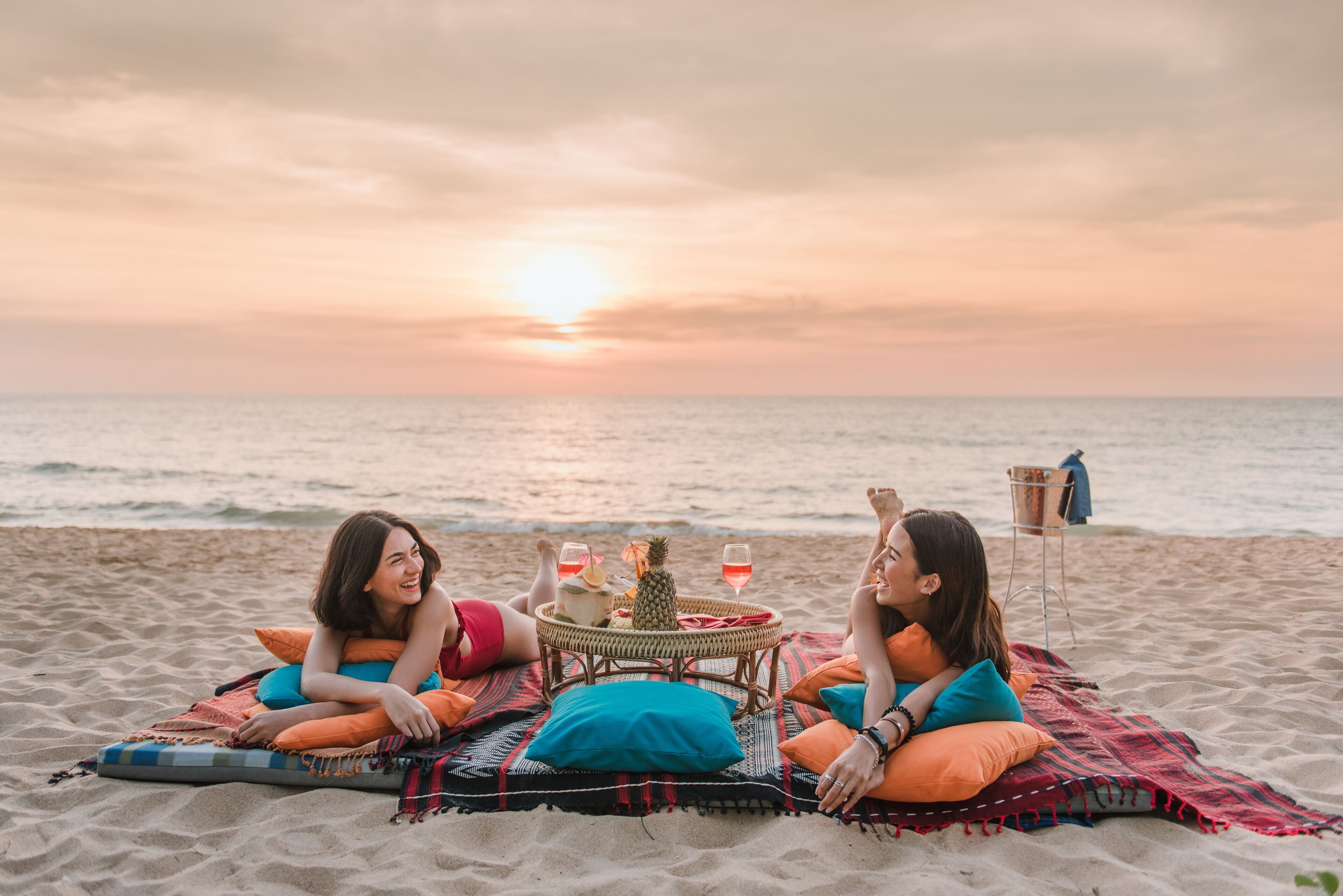 Two people relaxing on a beach with a table between them, featuring drinks and a pineapple.
