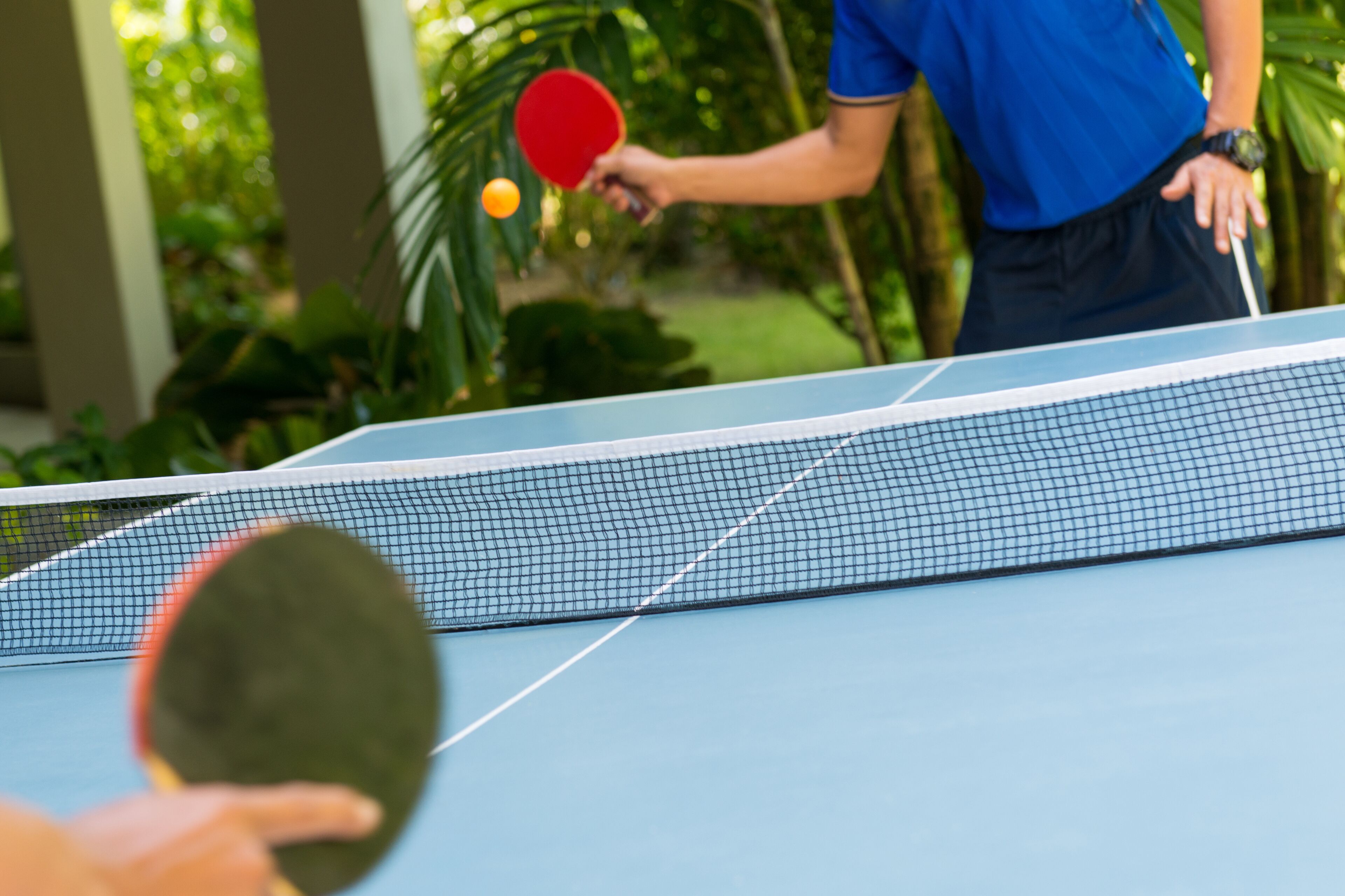 A table tennis table with a net, a red paddle, and a green paddle.