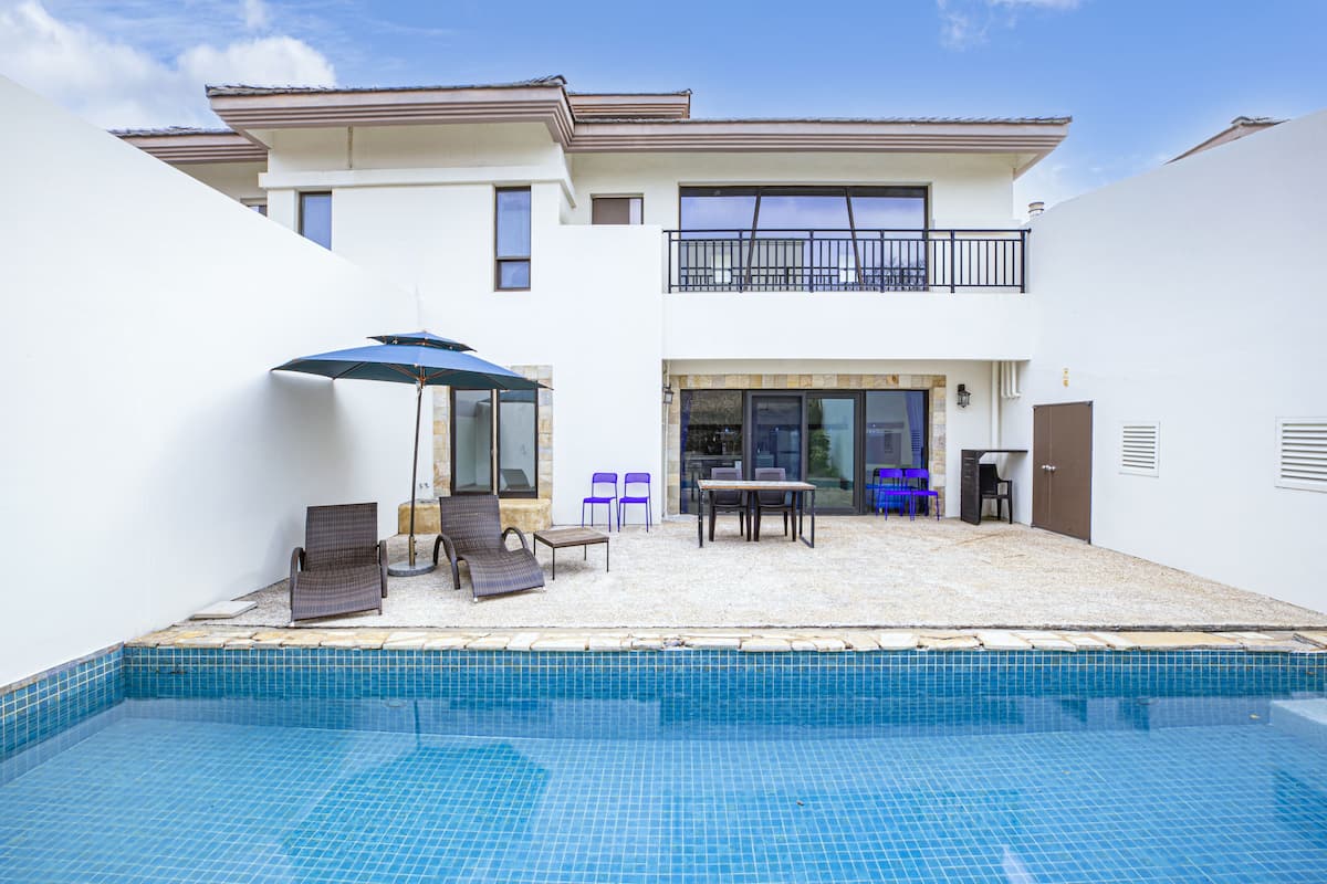A two-story house with a swimming pool, outdoor seating, and a balcony.
