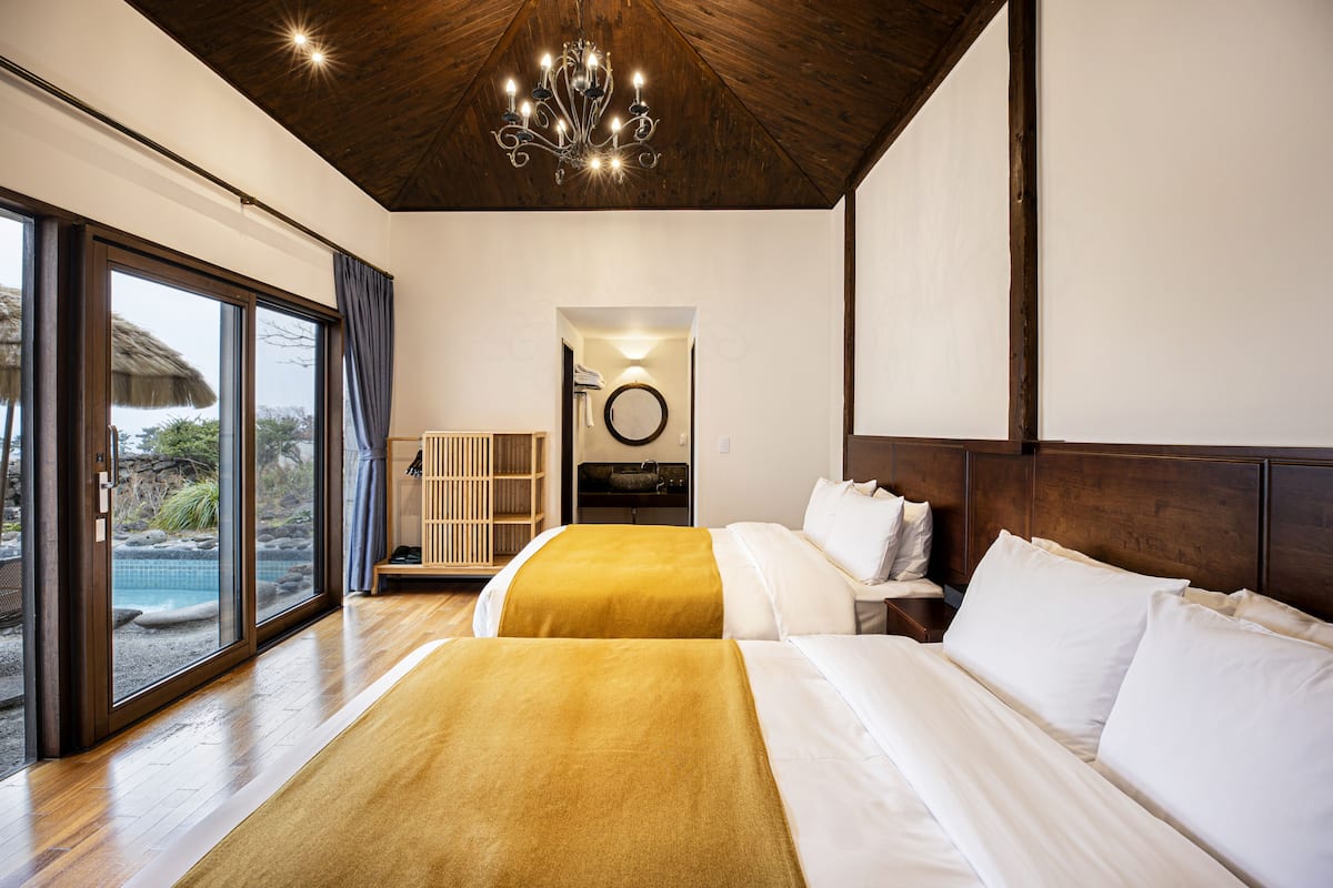 A hotel room with two beds, a large window with a view of a pool, and a wooden ceiling.