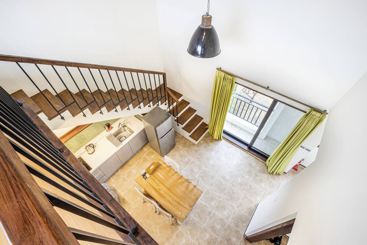 A spacious kitchen with a wooden table and chairs, a staircase with wooden railings, and a view of the balcony through a glass door.