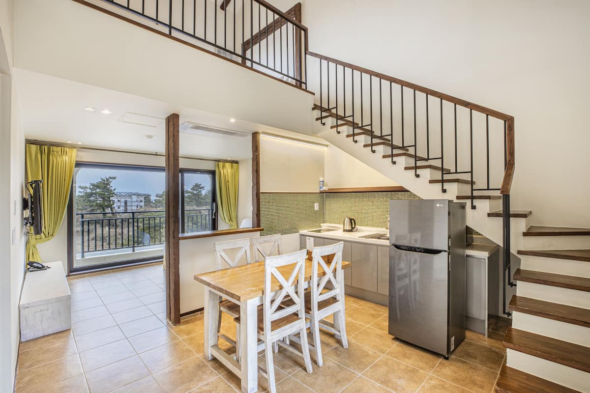 A kitchen with a dining table, chairs, a refrigerator, and a staircase.
