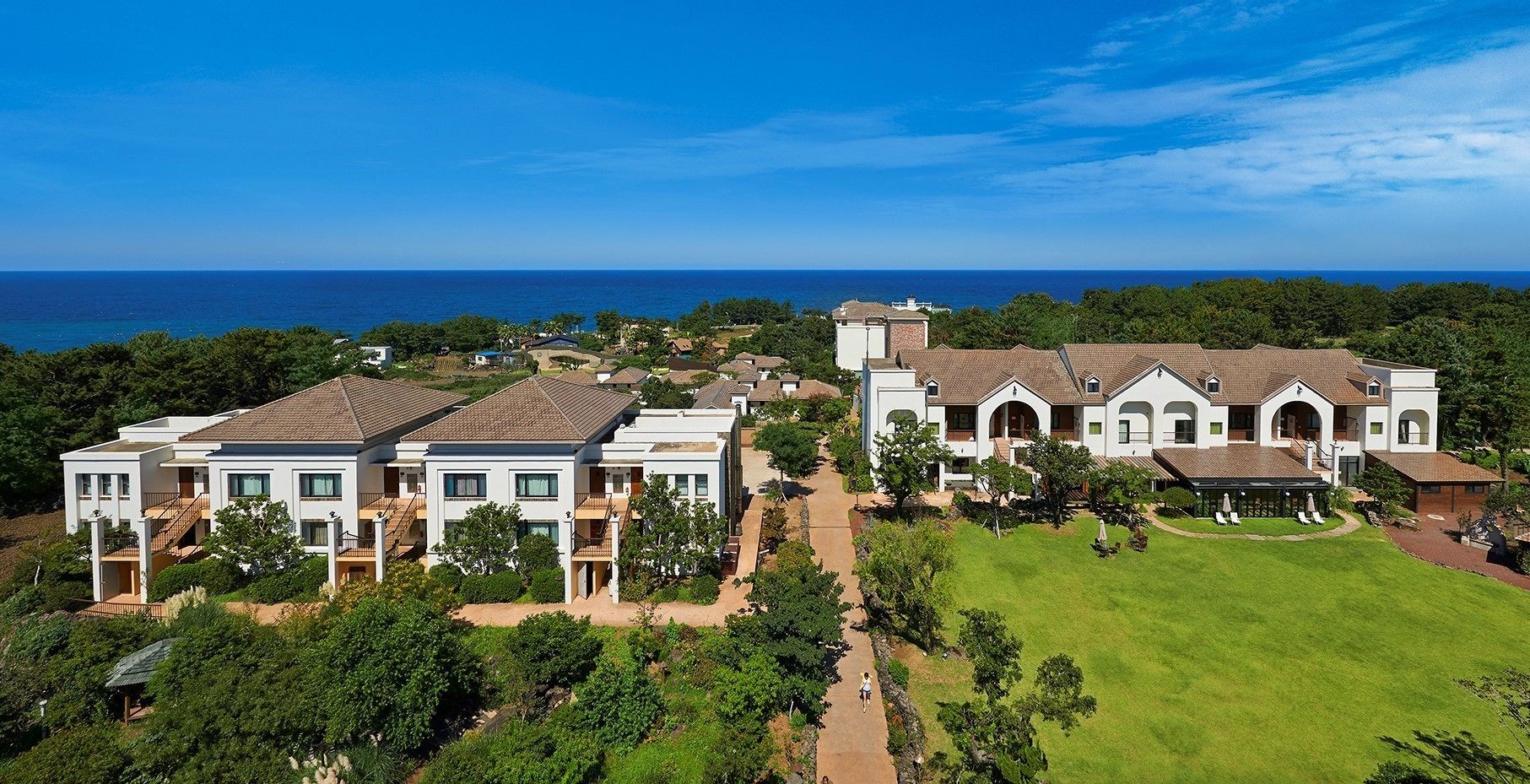 A large estate with multiple buildings, a well-maintained lawn, and a view of the ocean.