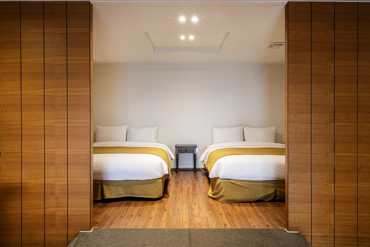A room with two beds, wooden flooring, and a small bedside table between them.