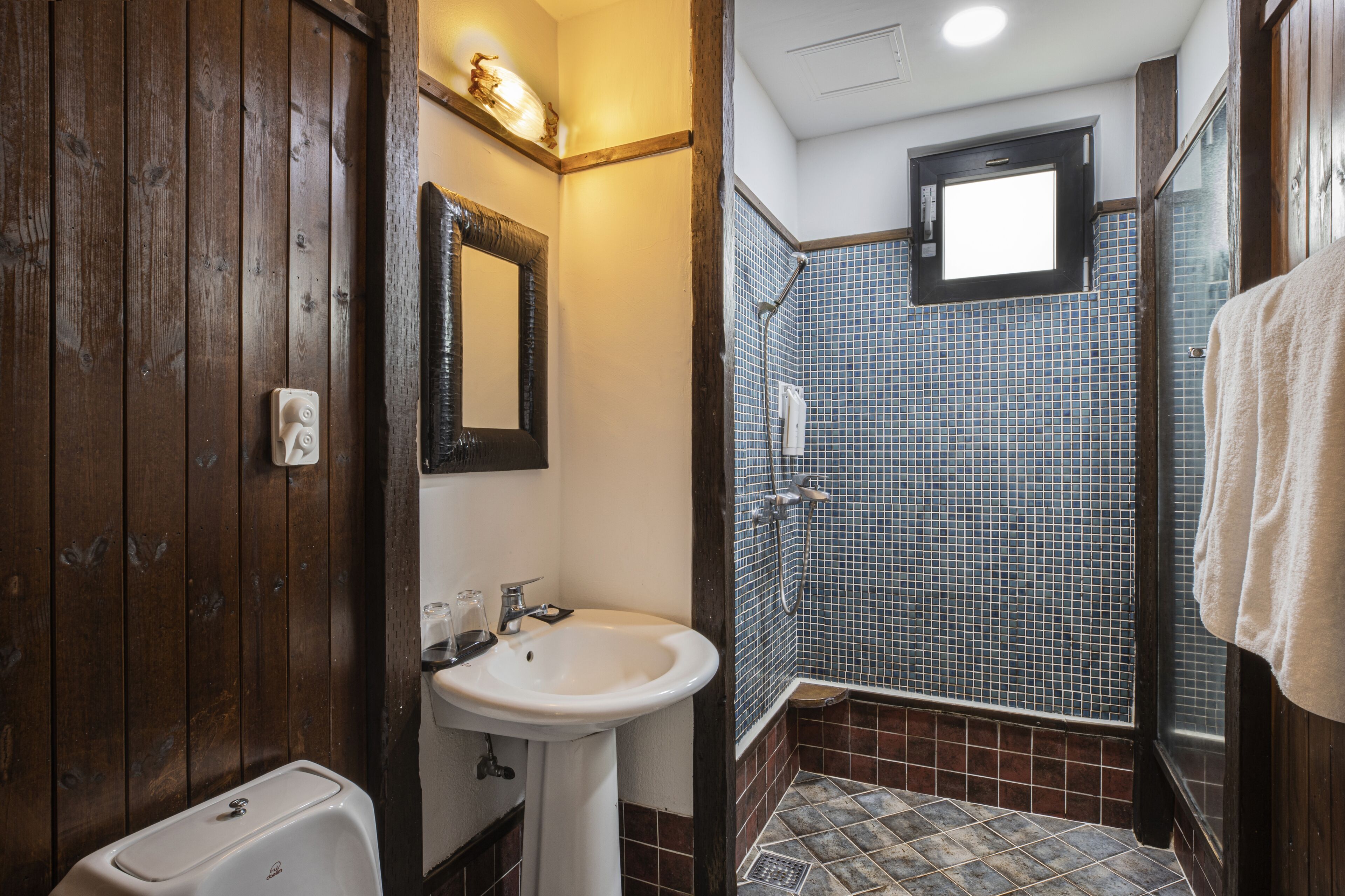 Un baño con tocador de madera, un lavabo blanco, un espejo y una zona de ducha con azulejos.