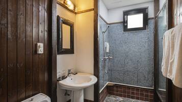 Un baño con tocador de madera, un lavabo blanco, un espejo y una zona de ducha con azulejos.