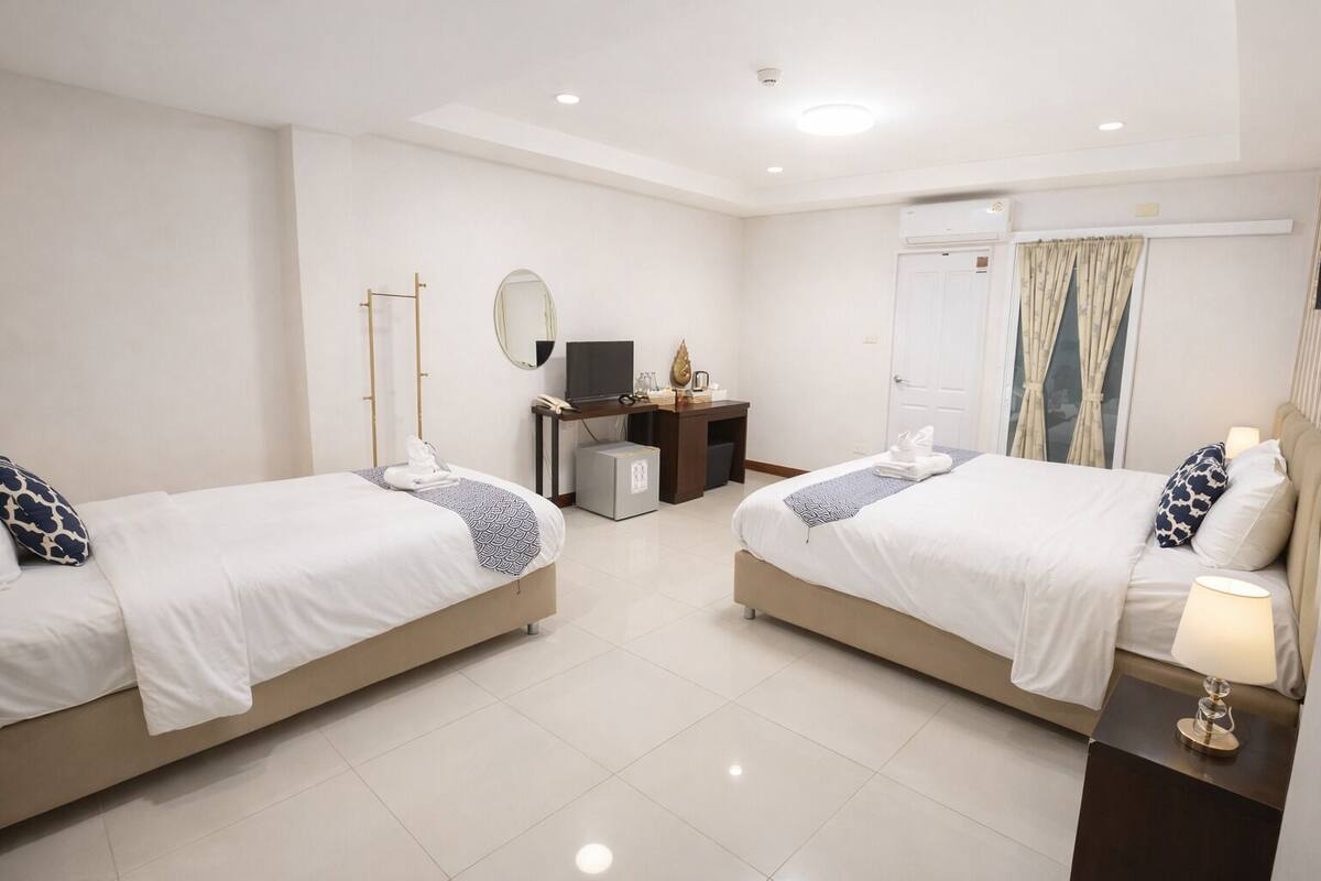 A hotel room with two beds, a desk with a computer, a mirror, and a door.