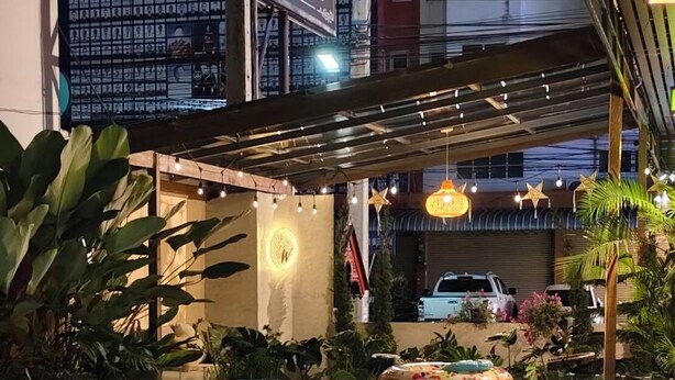 A swimming pool with a tiled deck, surrounded by plants and a covered area with string lights. - Chiang Mai Waroros Boutique Hotel (Chiang Mai)
