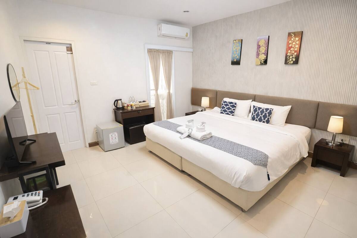 A hotel room with a large bed, bedside tables, a desk, a wardrobe, and an air conditioning unit.