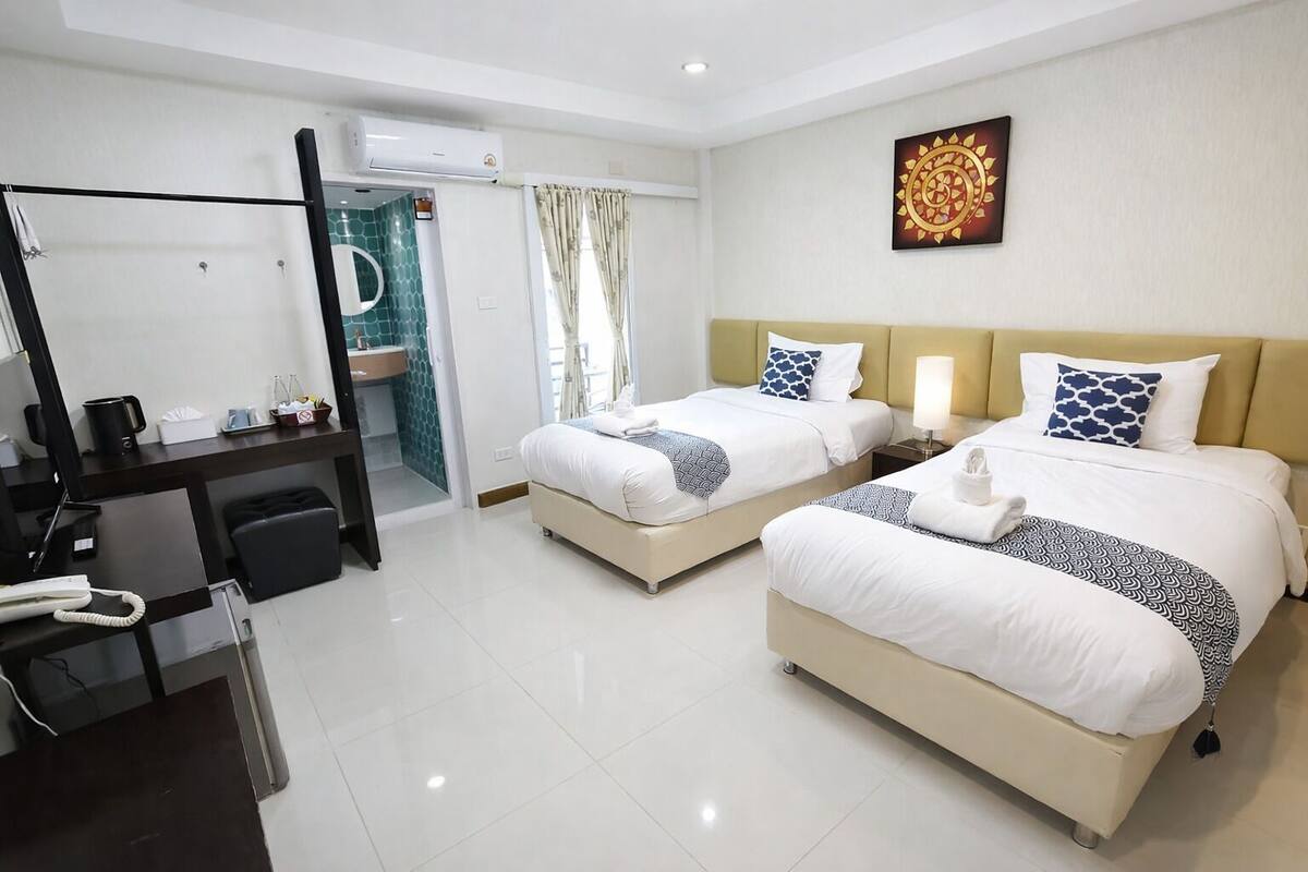 A hotel room with two beds, a desk, a mirror, and a bathroom visible through an open door.