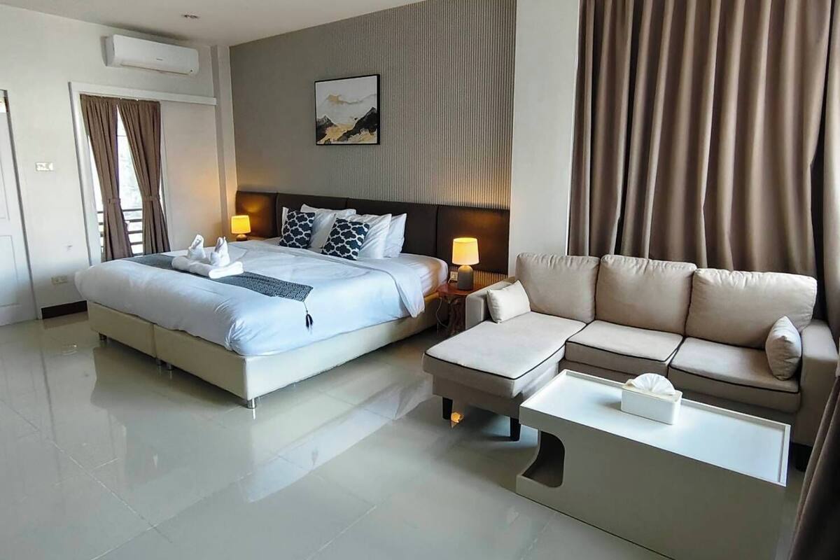 A hotel room with a bed, a sofa, a coffee table, and a wall-mounted air conditioner.