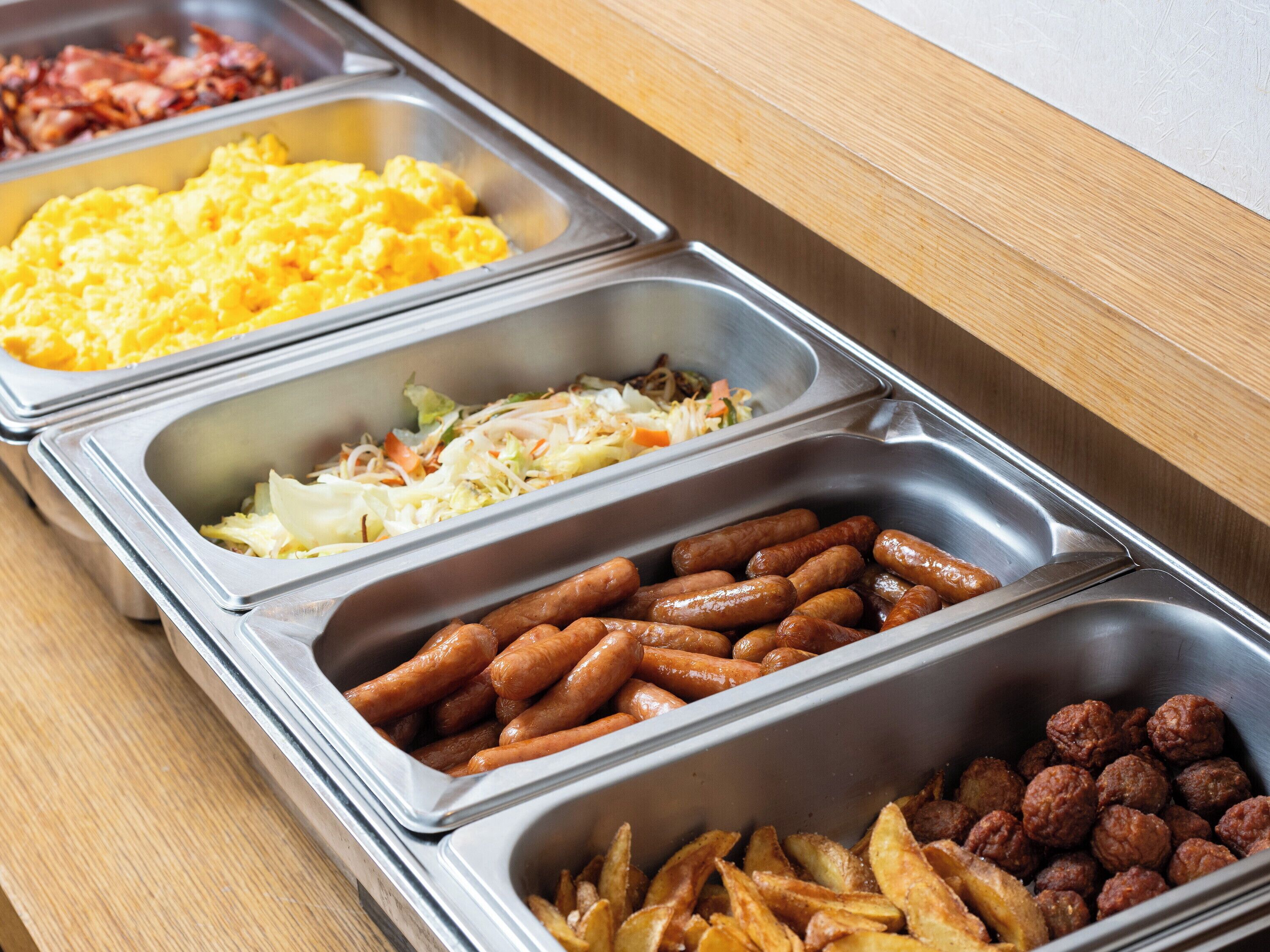 Un bufé con diversas opciones de comida, incluyendo huevos revueltos, ensalada de col, salchichas y albóndigas.