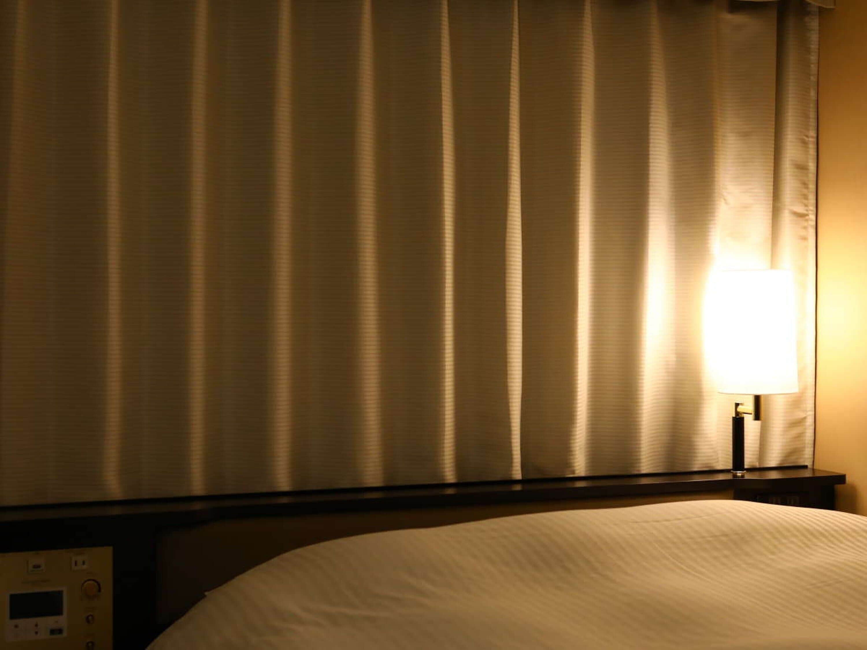 Una habitación de hotel con una cama, una mesita de noche con panel de control y una lámpara.