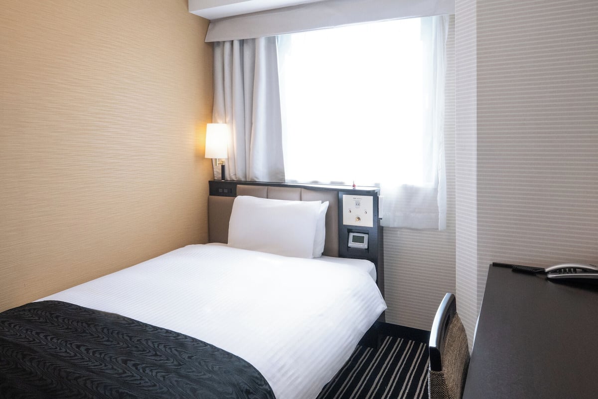 Une chambre d’hôtel avec un lit, un bureau et une fenêtre avec des rideaux.