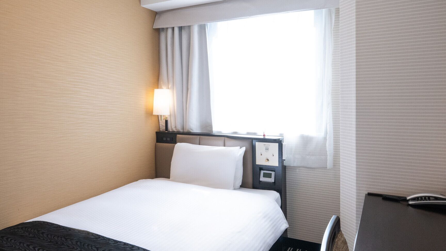 Une chambre d’hôtel avec un lit, un bureau, une lampe et une fenêtre avec des rideaux.