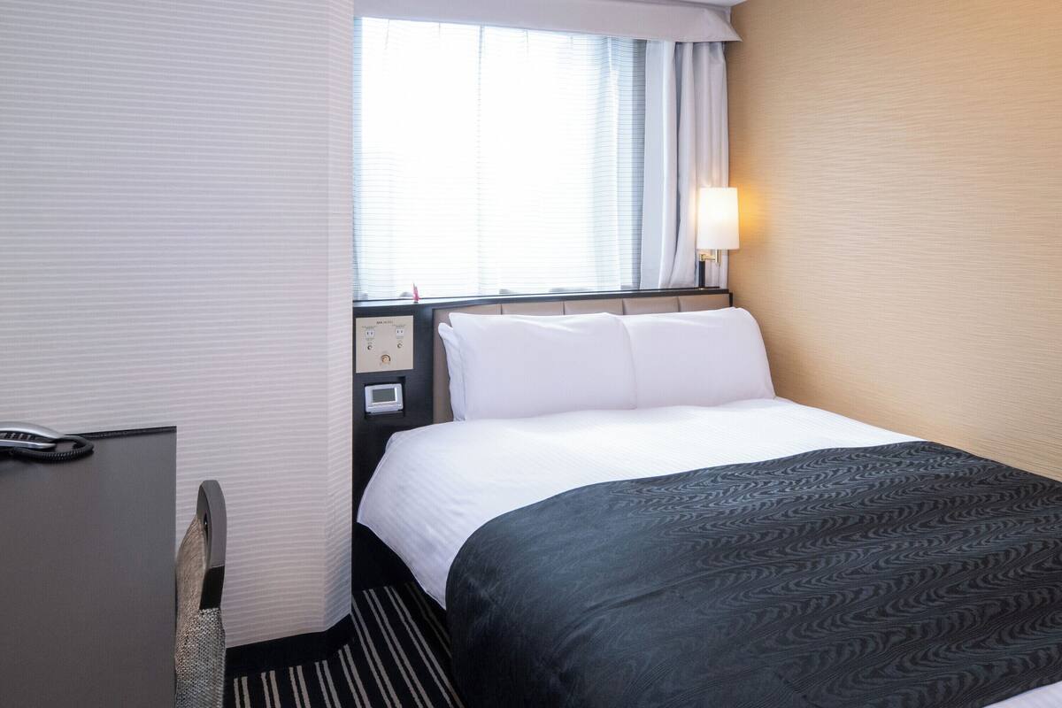 Une chambre d’hôtel avec un lit, une table de chevet, une lampe et une fenêtre avec des rideaux.