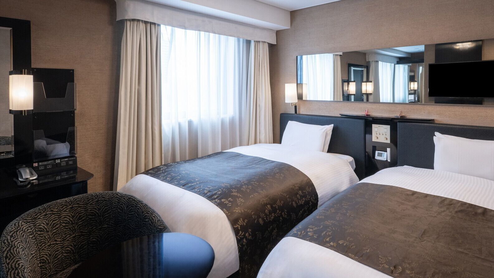 Une chambre d’hôtel avec deux lits, un bureau doté d’un téléviseur à écran plat, un miroir et une fenêtre avec des rideaux.
