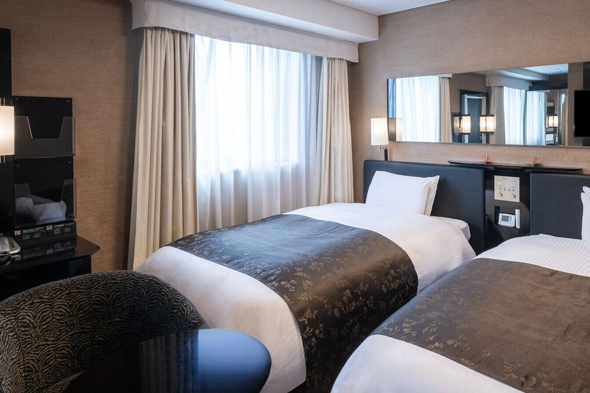 Une chambre d’hôtel avec deux lits, un bureau doté d’un téléviseur à écran plat, un miroir et une fenêtre avec des rideaux.