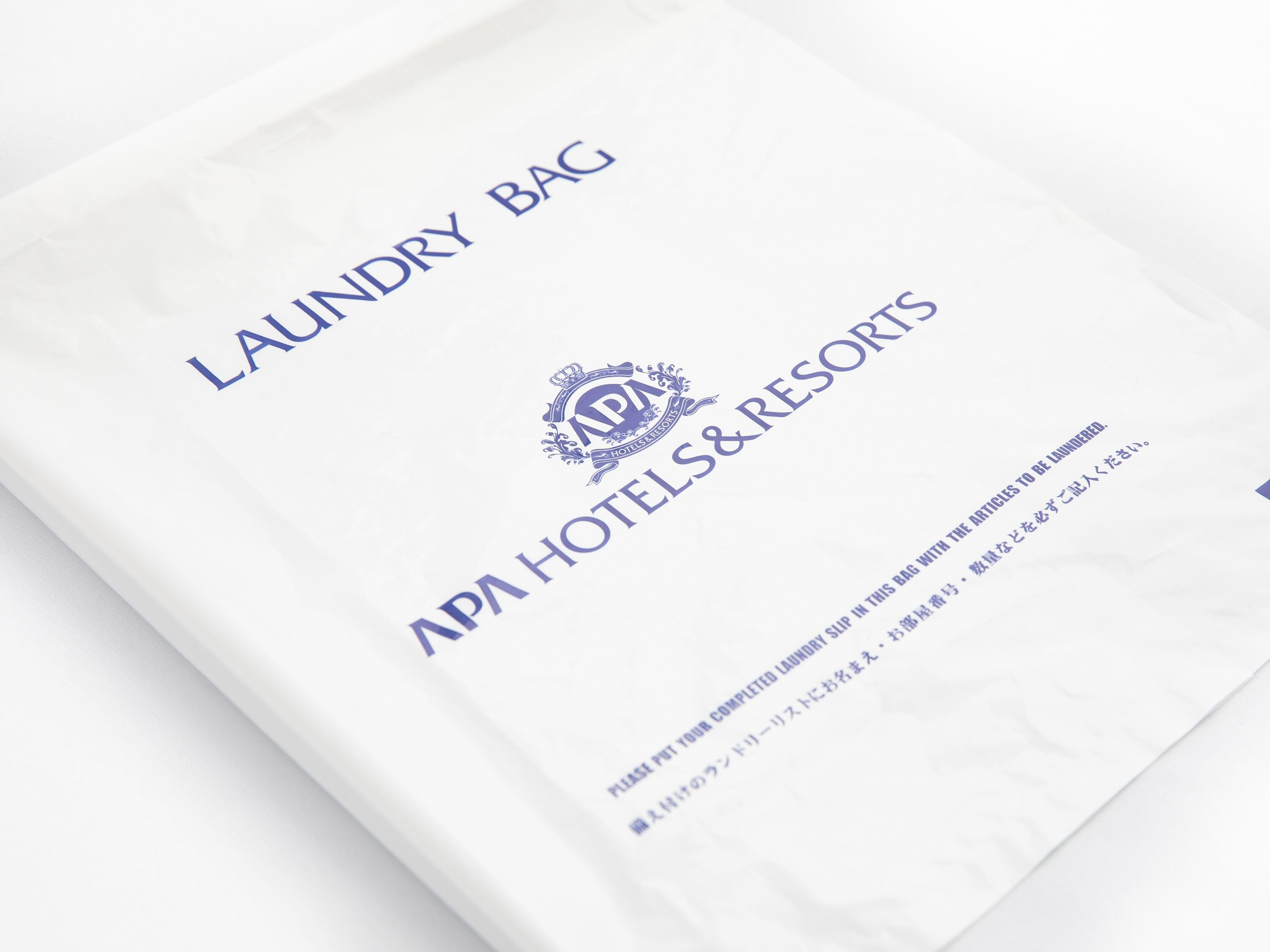 Ein weißer Wäschebeutel mit dem Aufdruck 'Laundry Bag' und 'APA Hotels & Resorts' sowie einem Logo.