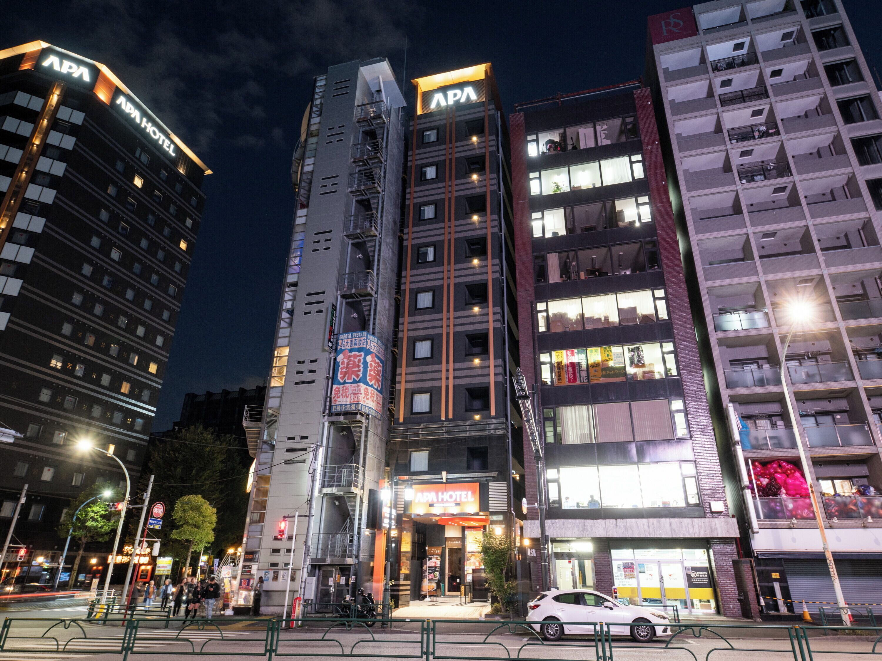 A multi-story building with "APA HOTEL" signage, a visible entrance, and a street view with pedestrians and vehicles.