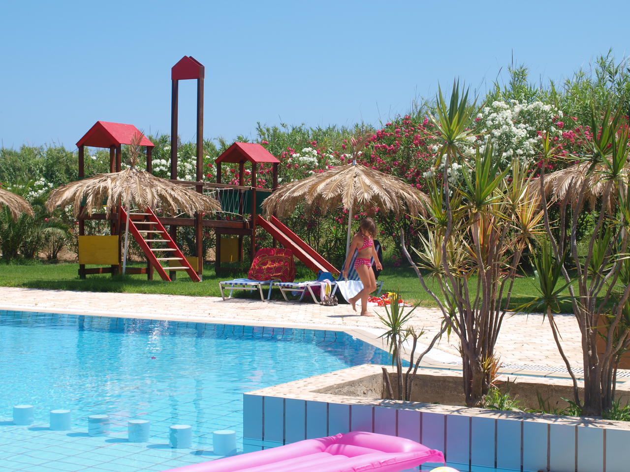 A swimming pool with a slide and a play structure with a red roof.