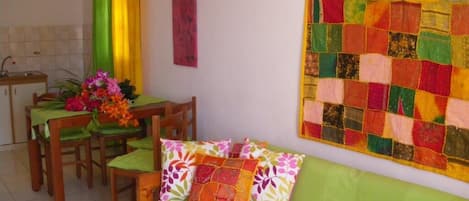 A cozy living room with a green sofa, a dining table with chairs, and a colorful quilt hanging on the wall.