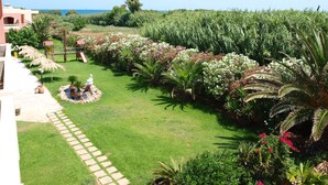 Un jardín cuidado con diversas plantas y un pequeño estanque, que conduce a un edificio con balcón con vistas al mar.