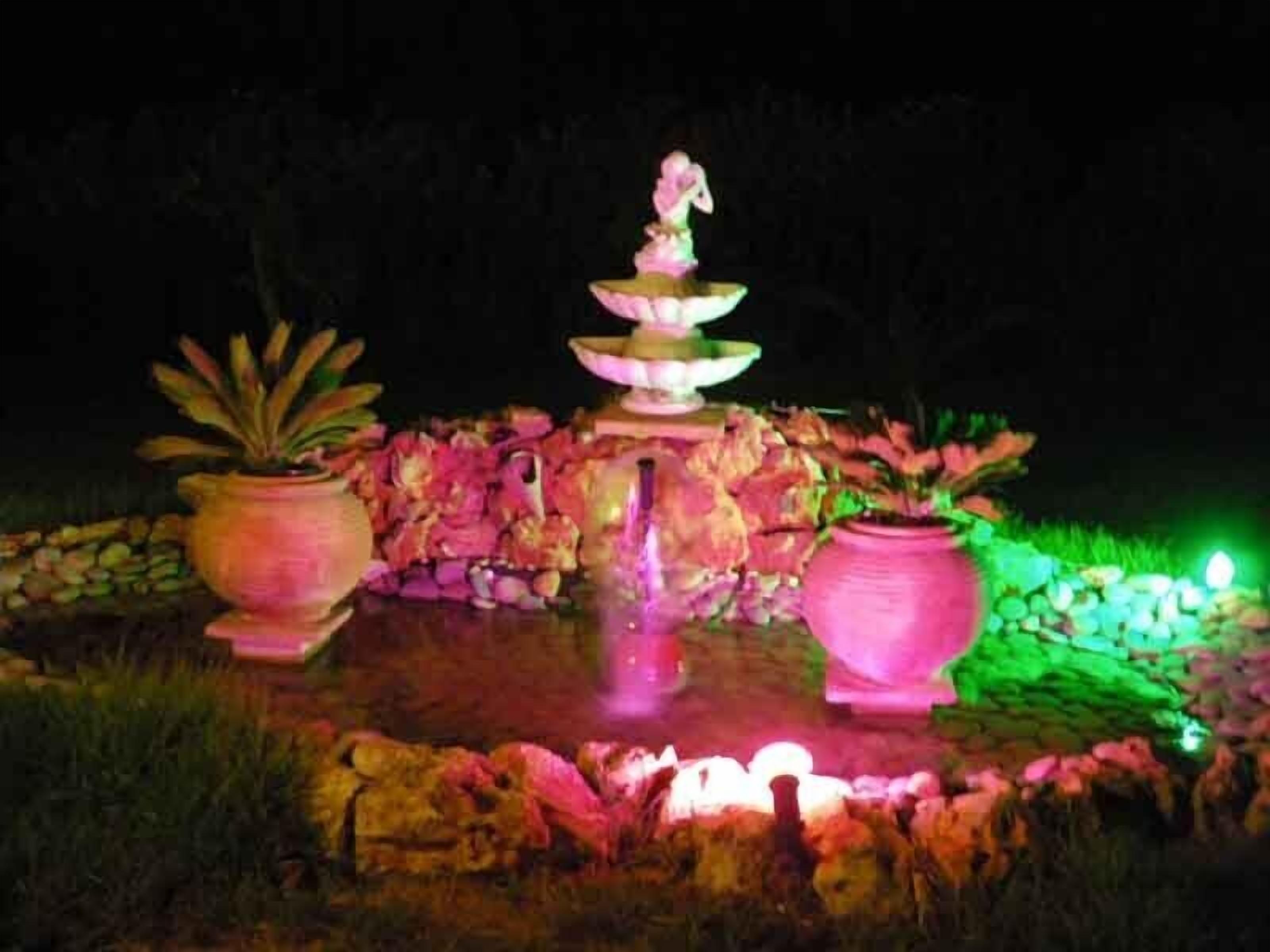 Ein nächtlicher Außenbrunnen mit gestuften Wasserspielen, beleuchtet mit pinken und grünen Lichtern.