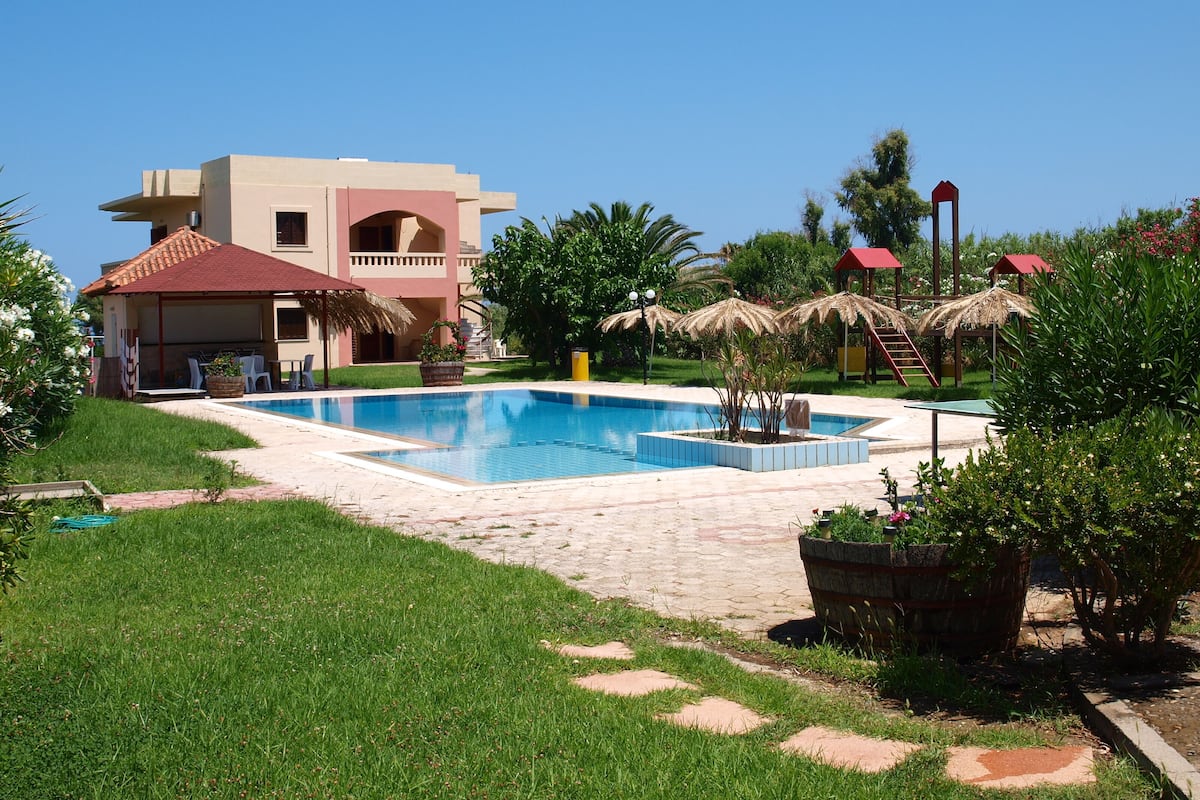 A swimming pool surrounded by a garden with a building in the background.