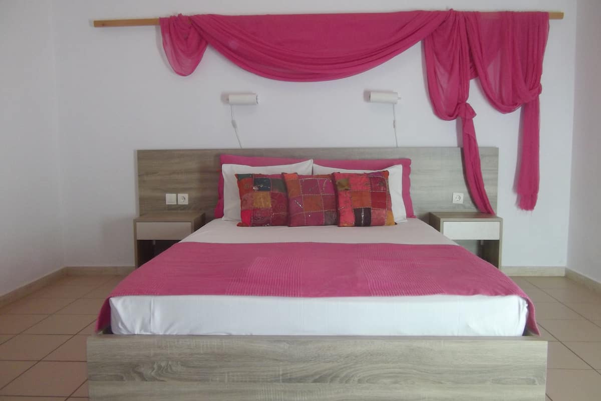 A bed with a wooden headboard, two bedside tables, and a pink canopy.