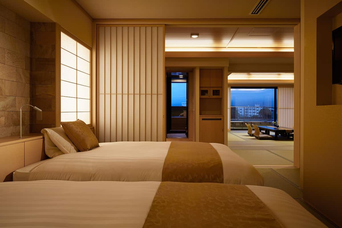 Une chambre d’hôtel avec deux lits, un paravent coulissant de style japonais, une vue sur la ville et un petit coin salon.