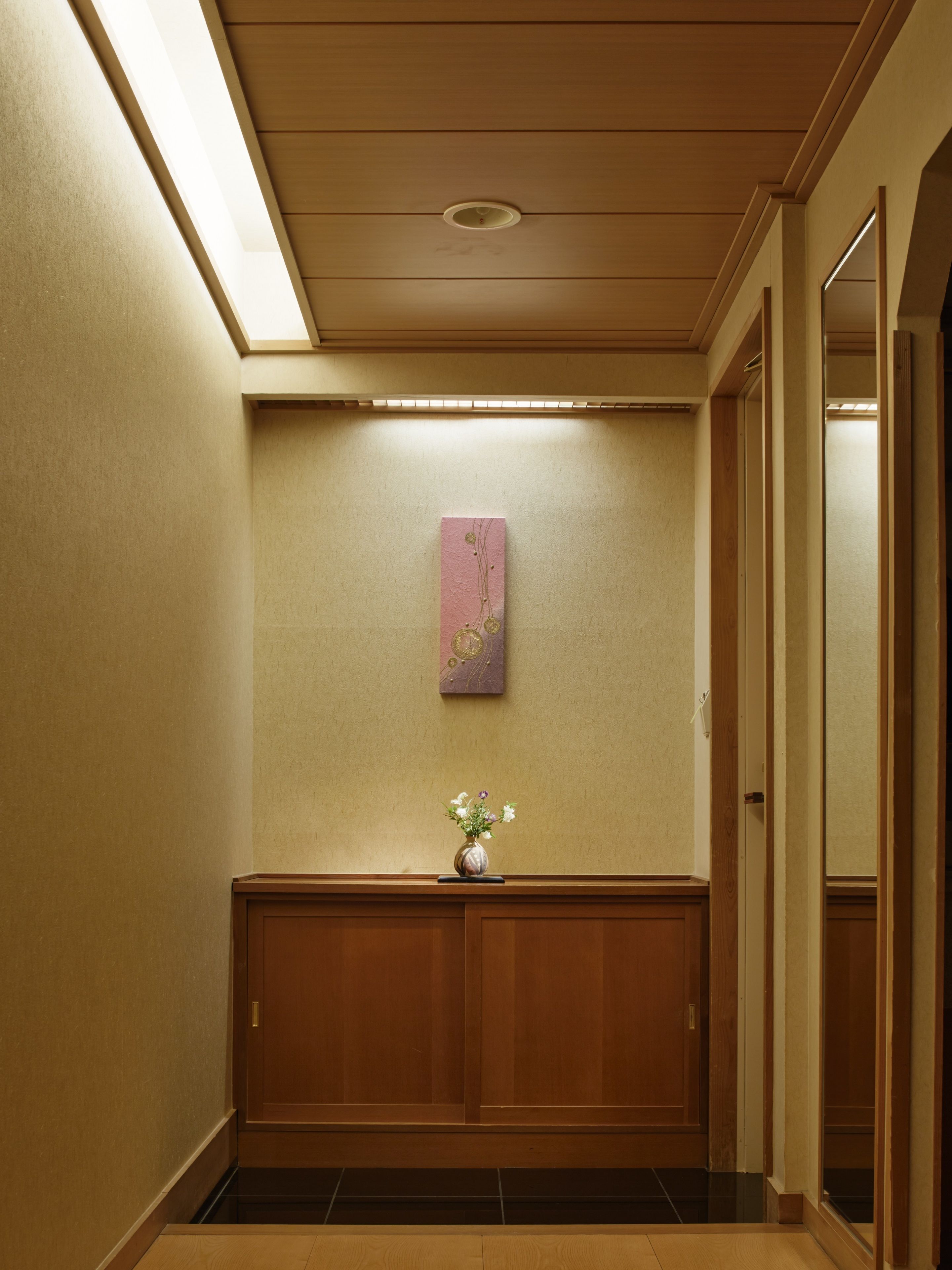 Un pasillo con una puerta de madera, una obra de arte en la pared y un florero con flores.