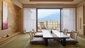 A traditional Japanese room with tatami flooring, a low table with cushions, and a view of a mountain through large sliding doors. - Konansou (Fujikawaguchiko)